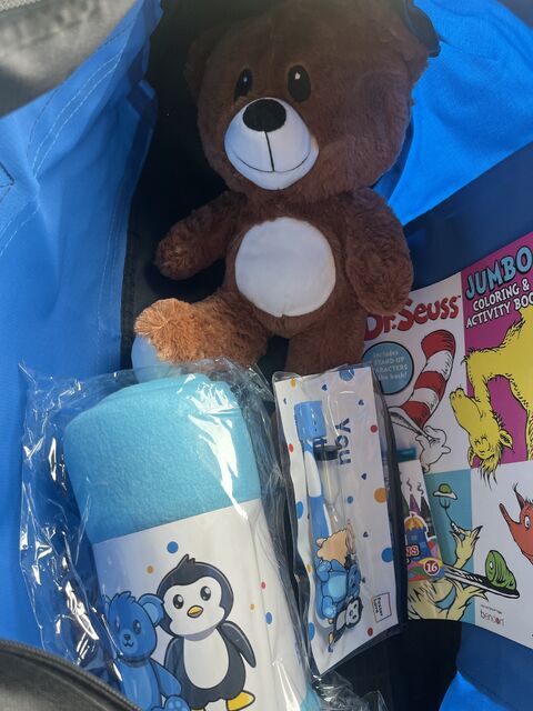 Duffle bag containing blank, toy bear, toiletries, and other goods for small child